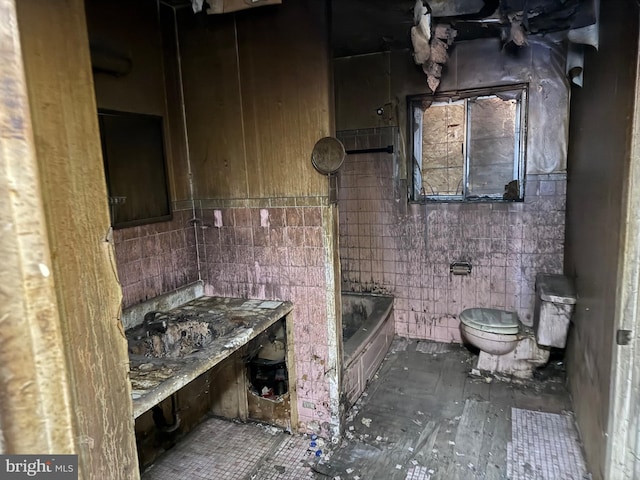 bathroom with a washtub, tile walls, and toilet