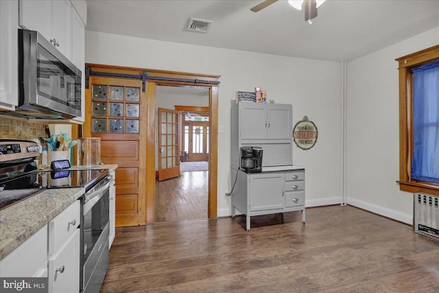 kitchen with radiator heating unit, tasteful backsplash, a barn door, white cabinets, and appliances with stainless steel finishes