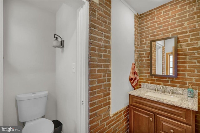 bathroom featuring vanity, brick wall, and toilet