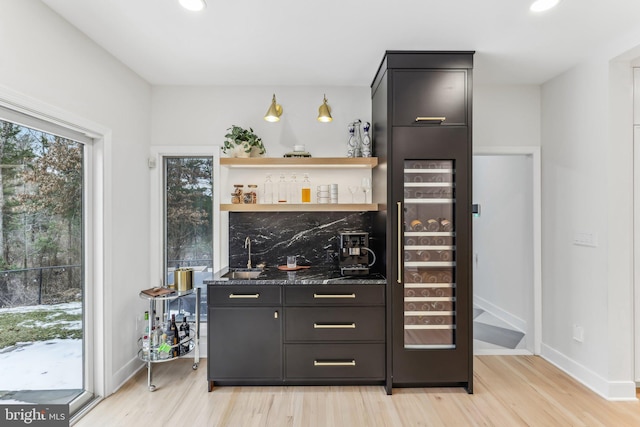 bar with sink, decorative backsplash, light hardwood / wood-style floors, and dark stone counters