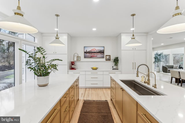 kitchen featuring sink, white cabinetry, light stone counters, hanging light fixtures, and light hardwood / wood-style floors