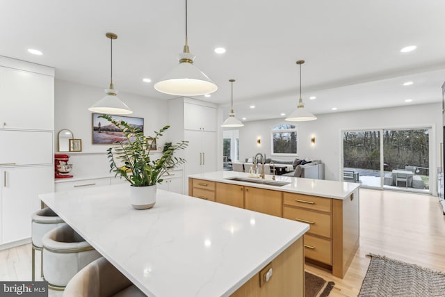 kitchen with sink, white cabinetry, hanging light fixtures, a spacious island, and light hardwood / wood-style floors