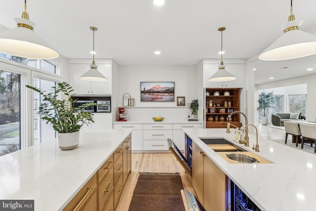 kitchen with pendant lighting, sink, white cabinets, light stone countertops, and light wood-type flooring