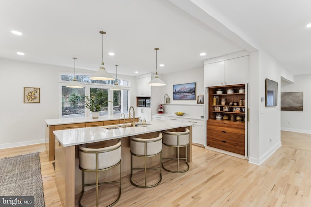 kitchen featuring a kitchen bar, sink, white cabinetry, hanging light fixtures, and a center island with sink