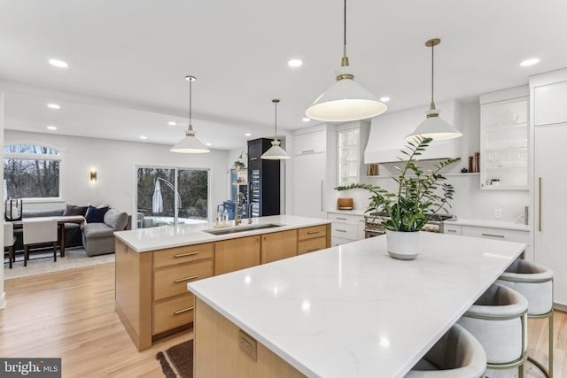 kitchen with sink, decorative light fixtures, light wood-type flooring, a large island, and white cabinets