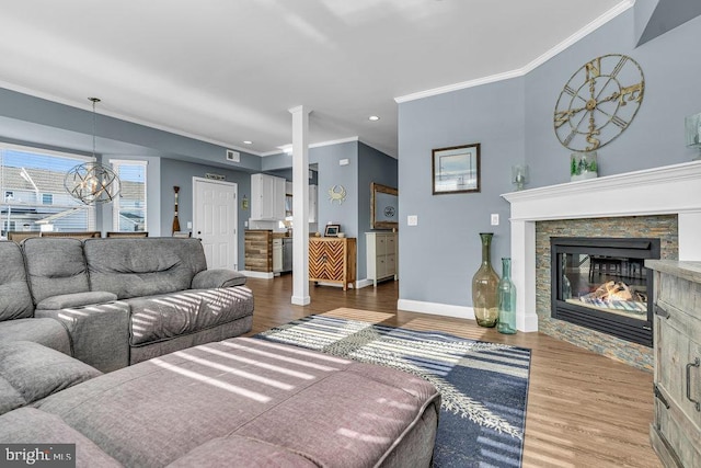 living room featuring a chandelier, wood-type flooring, a stone fireplace, and ornamental molding