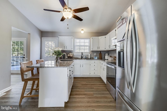 kitchen featuring white cabinetry, stainless steel appliances, dark stone counters, a breakfast bar area, and a kitchen island