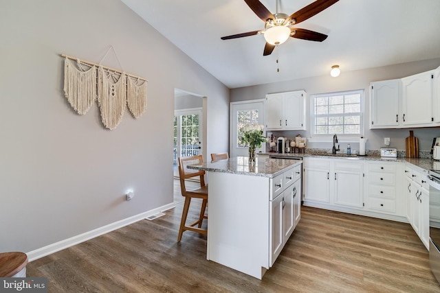 kitchen featuring light stone countertops, sink, white cabinets, a center island, and light hardwood / wood-style floors