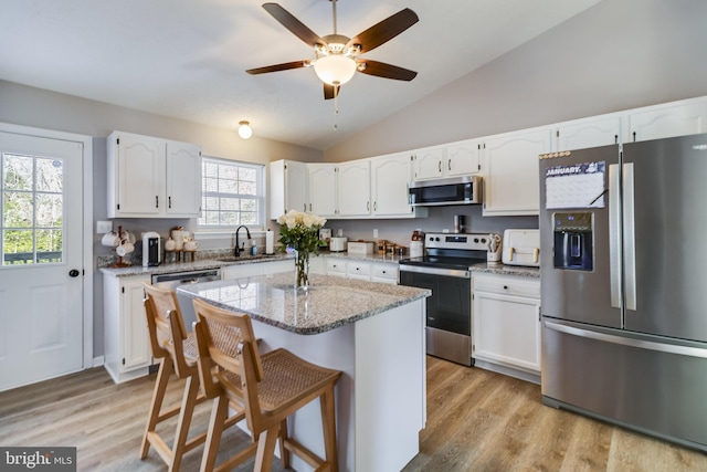 kitchen with a center island, sink, stainless steel appliances, vaulted ceiling, and white cabinets