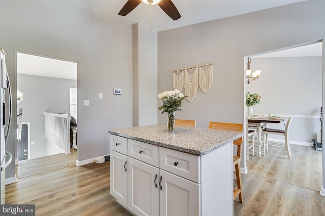 kitchen featuring a kitchen breakfast bar, ceiling fan, light stone countertops, light hardwood / wood-style floors, and white cabinetry