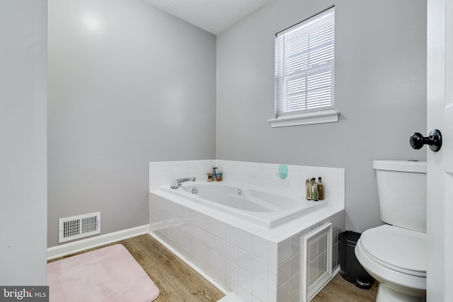 bathroom featuring hardwood / wood-style floors, a relaxing tiled tub, and toilet