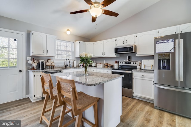 kitchen featuring a kitchen bar, stainless steel appliances, vaulted ceiling, a kitchen island, and white cabinetry