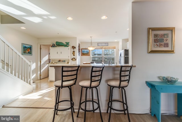 kitchen with hanging light fixtures, light hardwood / wood-style floors, stainless steel fridge, a breakfast bar, and white cabinetry