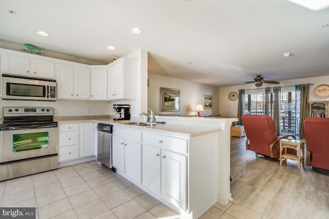 kitchen with appliances with stainless steel finishes, kitchen peninsula, ceiling fan, white cabinets, and sink