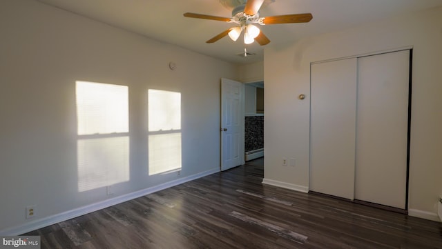 unfurnished bedroom featuring a closet, dark hardwood / wood-style flooring, baseboard heating, and ceiling fan