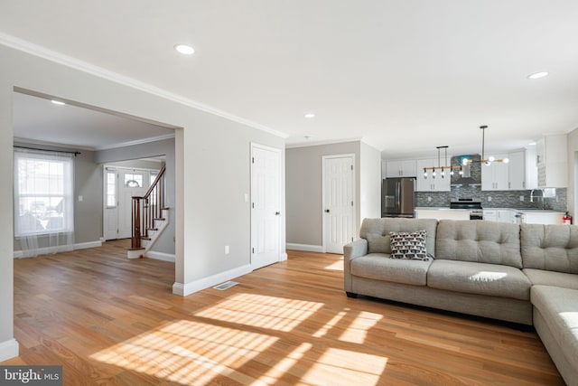 living room with sink, an inviting chandelier, light wood-type flooring, and crown molding