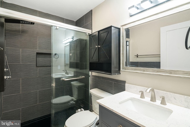 bathroom featuring tile walls, a shower with door, vanity, and toilet