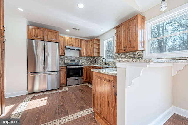 kitchen featuring stainless steel appliances, light stone counters, a kitchen bar, wood-type flooring, and backsplash