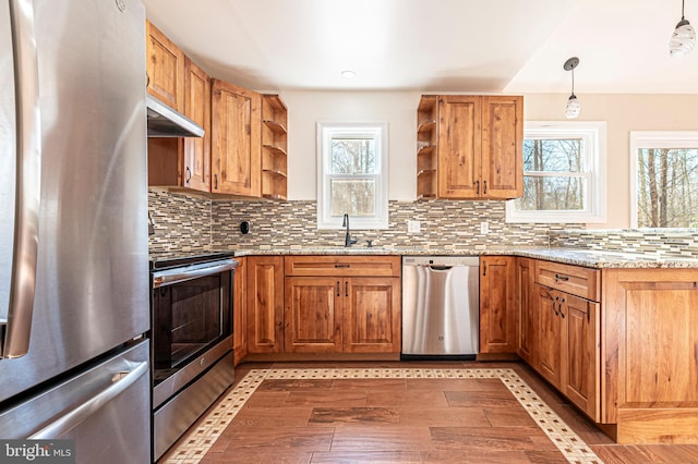 kitchen with decorative light fixtures, appliances with stainless steel finishes, light stone counters, and sink