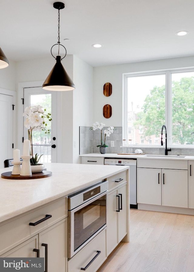 kitchen featuring dishwasher, sink, decorative light fixtures, decorative backsplash, and white cabinets