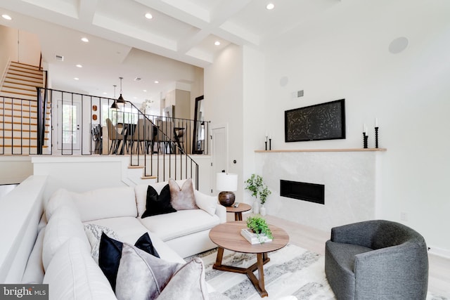 living room with beamed ceiling, light hardwood / wood-style flooring, a high ceiling, and coffered ceiling