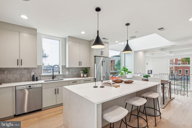 kitchen with sink, decorative backsplash, decorative light fixtures, a kitchen island, and stainless steel appliances