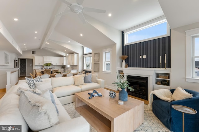 living room with ceiling fan, vaulted ceiling with beams, and plenty of natural light