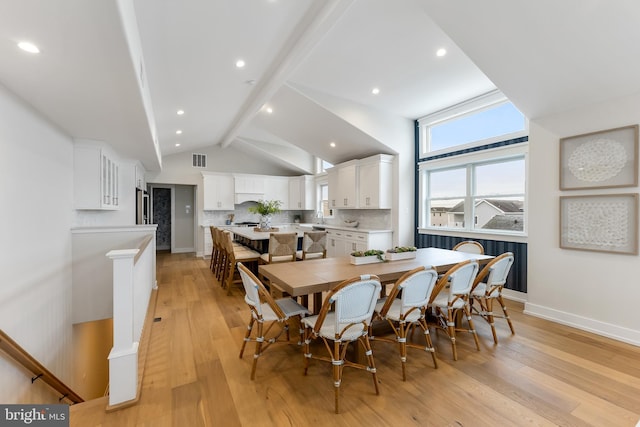 dining room featuring vaulted ceiling with beams and light hardwood / wood-style flooring