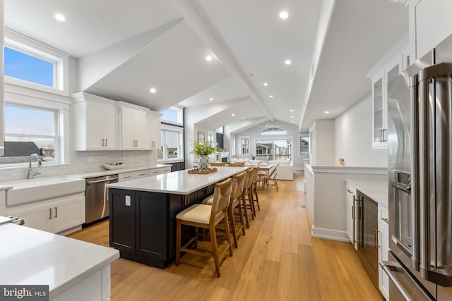 kitchen with vaulted ceiling, appliances with stainless steel finishes, a breakfast bar, a kitchen island, and white cabinets