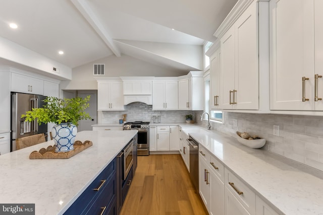 kitchen with stainless steel appliances, blue cabinetry, light stone counters, white cabinetry, and tasteful backsplash