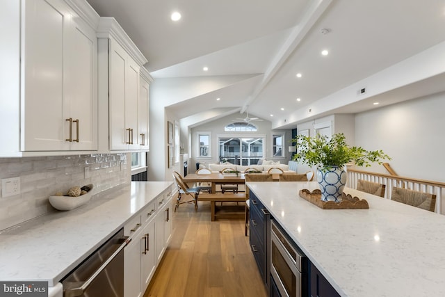 kitchen with white cabinets, vaulted ceiling, light stone counters, and appliances with stainless steel finishes