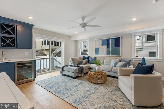 living room with ceiling fan, light hardwood / wood-style flooring, indoor wet bar, and wine cooler