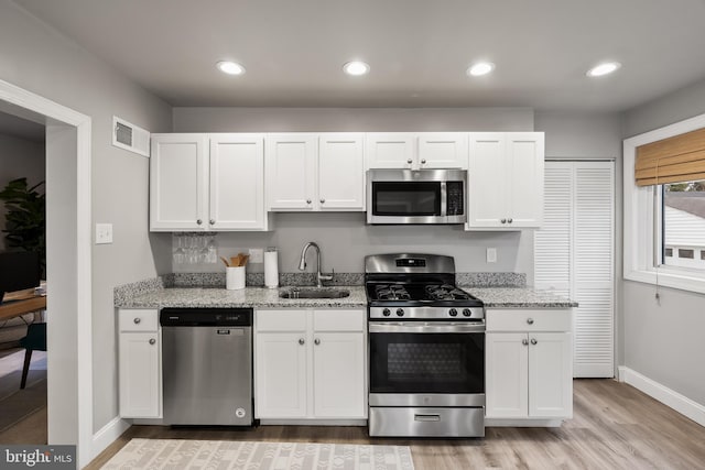 kitchen with sink, light stone countertops, appliances with stainless steel finishes, and white cabinetry