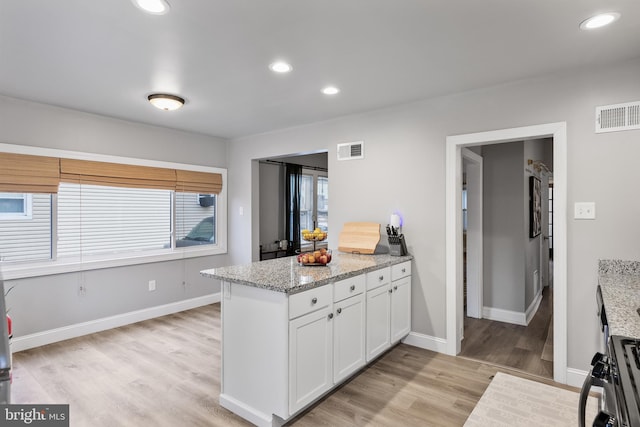 kitchen with range with gas stovetop, white cabinetry, light wood-type flooring, and light stone counters