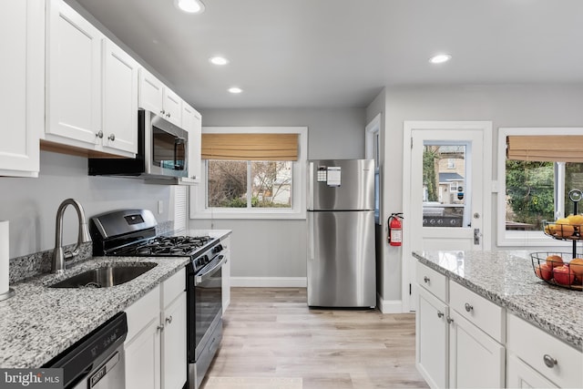 kitchen featuring appliances with stainless steel finishes, light hardwood / wood-style floors, white cabinets, and light stone counters