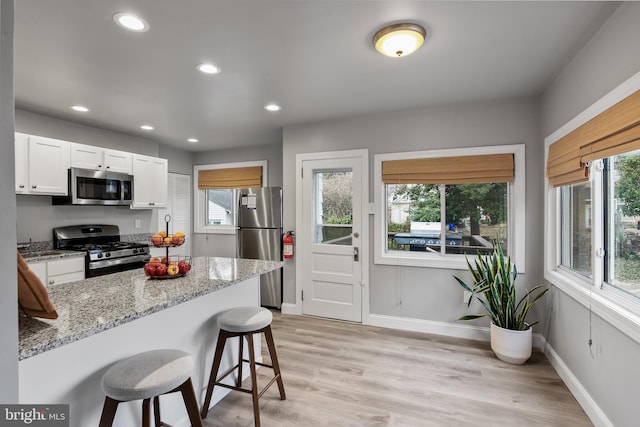 kitchen with light stone counters, light wood-type flooring, a breakfast bar area, appliances with stainless steel finishes, and white cabinetry