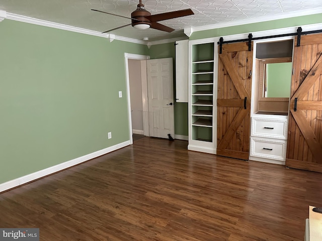 unfurnished bedroom with ceiling fan, a barn door, dark hardwood / wood-style flooring, and crown molding