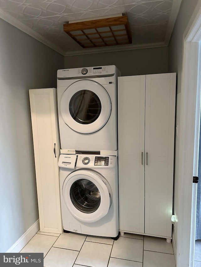 clothes washing area featuring light tile patterned flooring, crown molding, and stacked washer and dryer