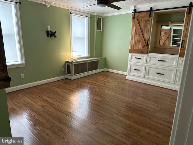 unfurnished bedroom featuring a barn door, dark hardwood / wood-style floors, ceiling fan, and ornamental molding