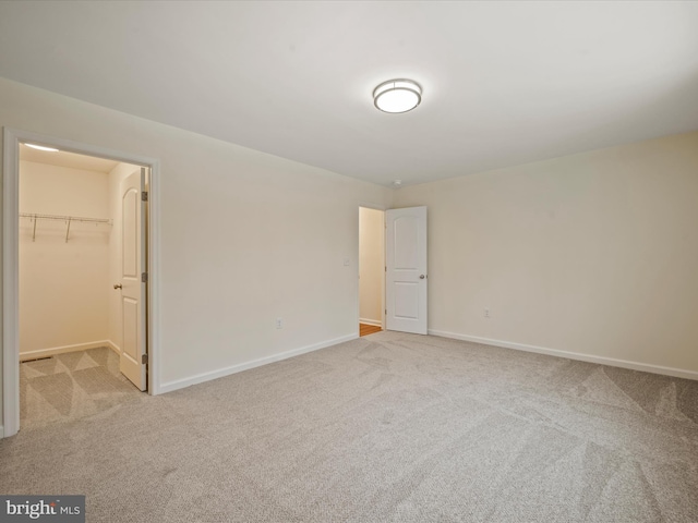 unfurnished bedroom featuring a walk in closet, light colored carpet, and a closet