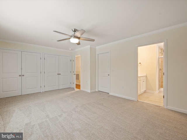 unfurnished bedroom featuring crown molding, ensuite bath, ceiling fan, and two closets