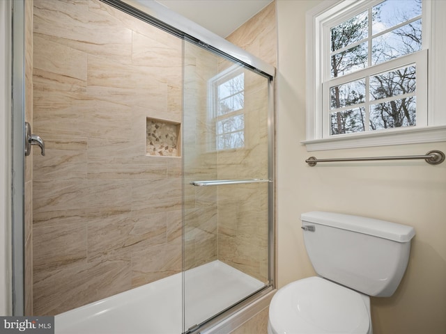 bathroom featuring a shower with door and toilet