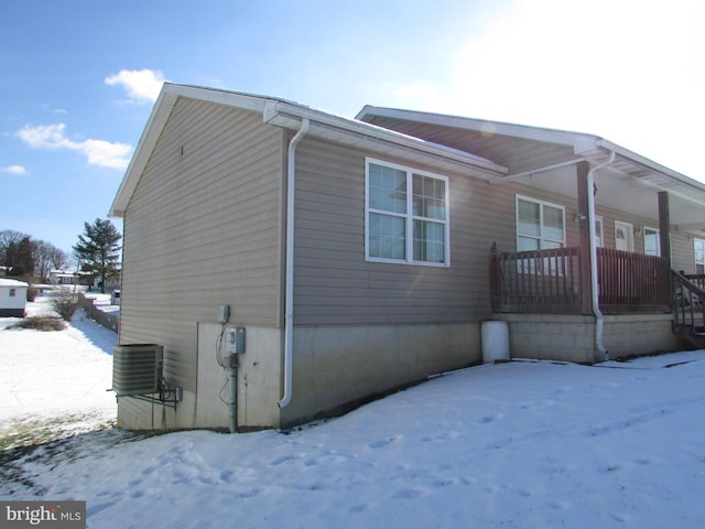 snow covered property with covered porch and central AC unit