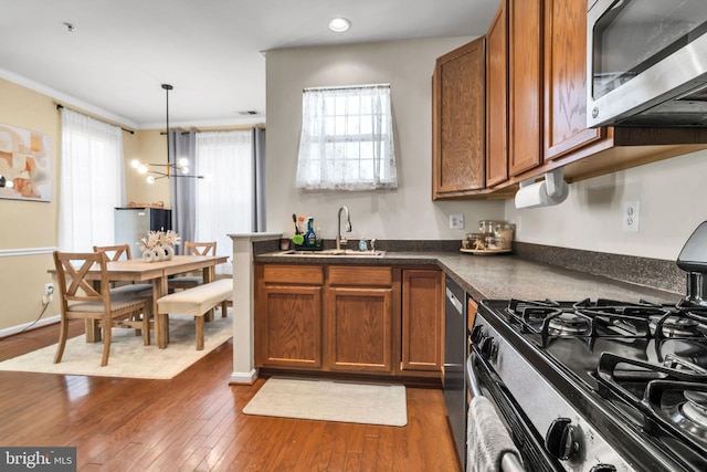 kitchen featuring dark wood-style flooring, stainless steel appliances, dark countertops, brown cabinetry, and a sink