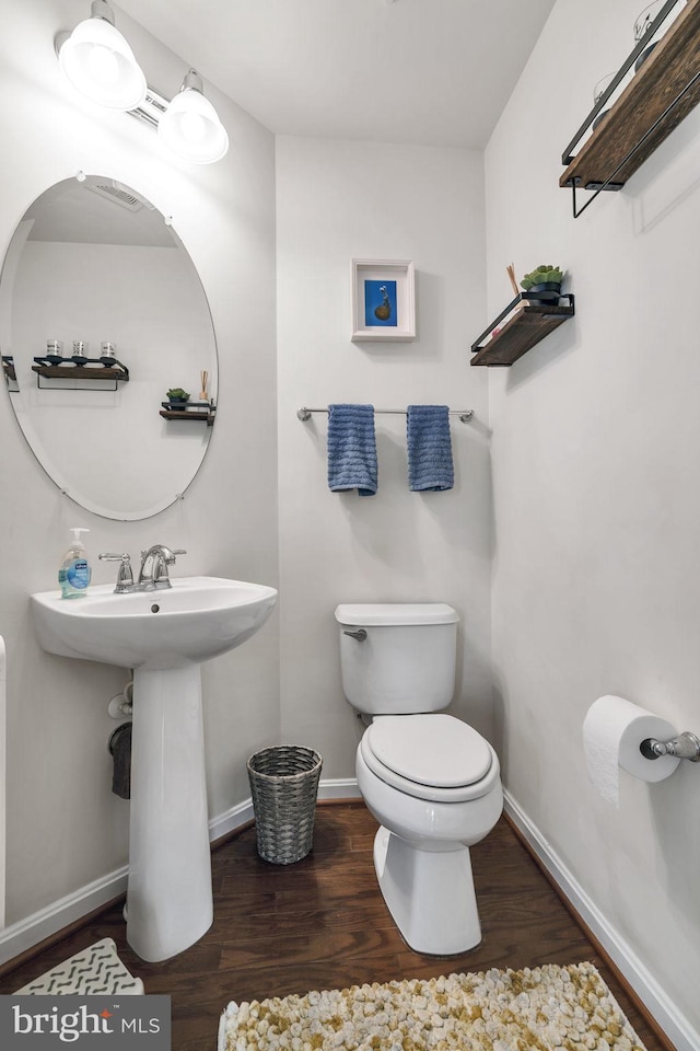 half bath with toilet, baseboards, and wood finished floors