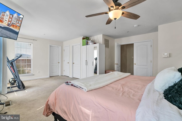 carpeted bedroom with a ceiling fan, two closets, visible vents, and baseboards