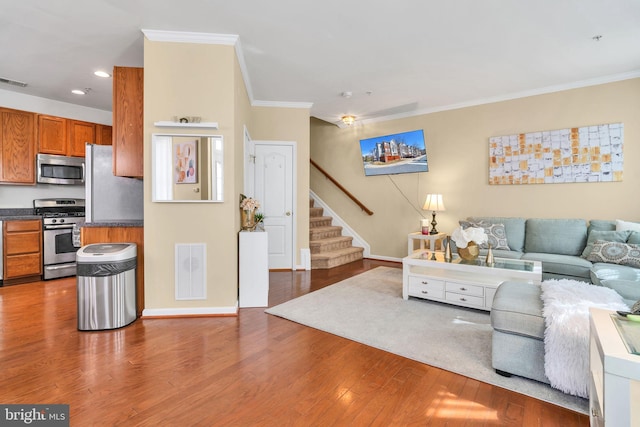 living area with ornamental molding, wood finished floors, visible vents, and stairs