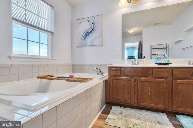 full bathroom featuring wood finished floors, a garden tub, a sink, and double vanity