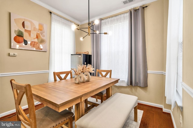 dining room featuring baseboards, visible vents, ornamental molding, wood finished floors, and a chandelier