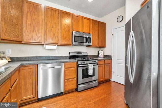 kitchen with dark countertops, light wood finished floors, appliances with stainless steel finishes, and brown cabinetry